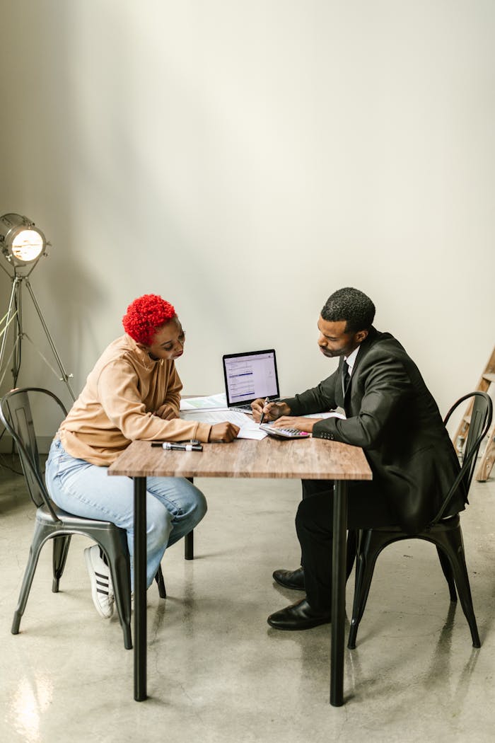 Two professionals collaborate in a bright modern office setting with a laptop and documents.